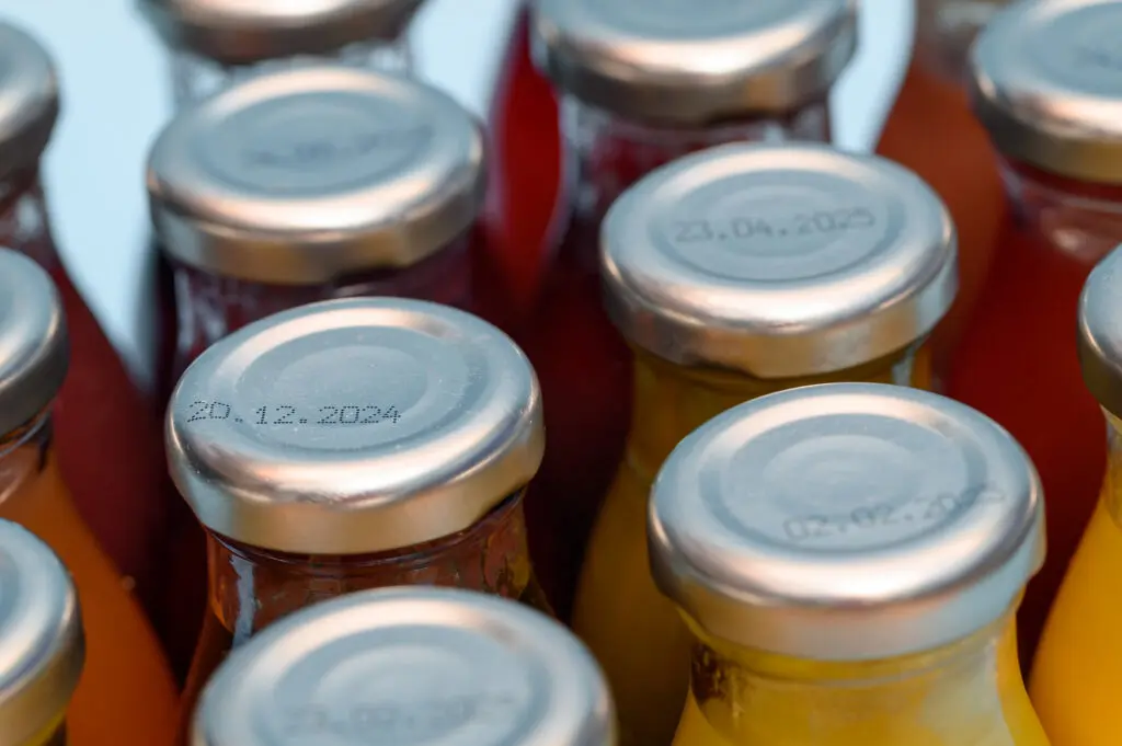 Close-up of printed expiration dates on fruit juices packaged in glass bottles with metal caps