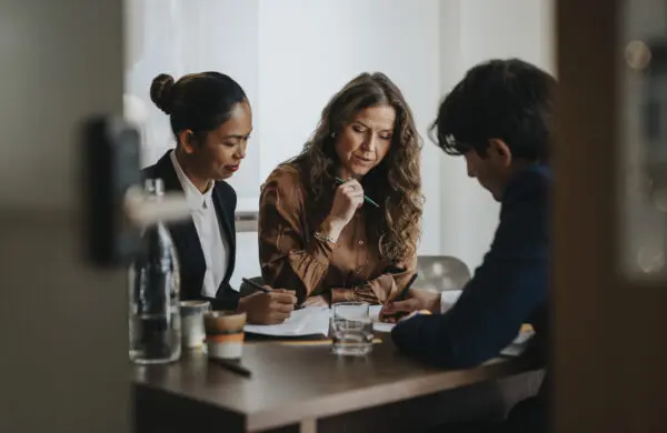 Young businessman writing while discussing strategy with female colleagues sitting at desk in office