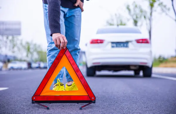 Man setting down red warning triangle on road in front of stalled car