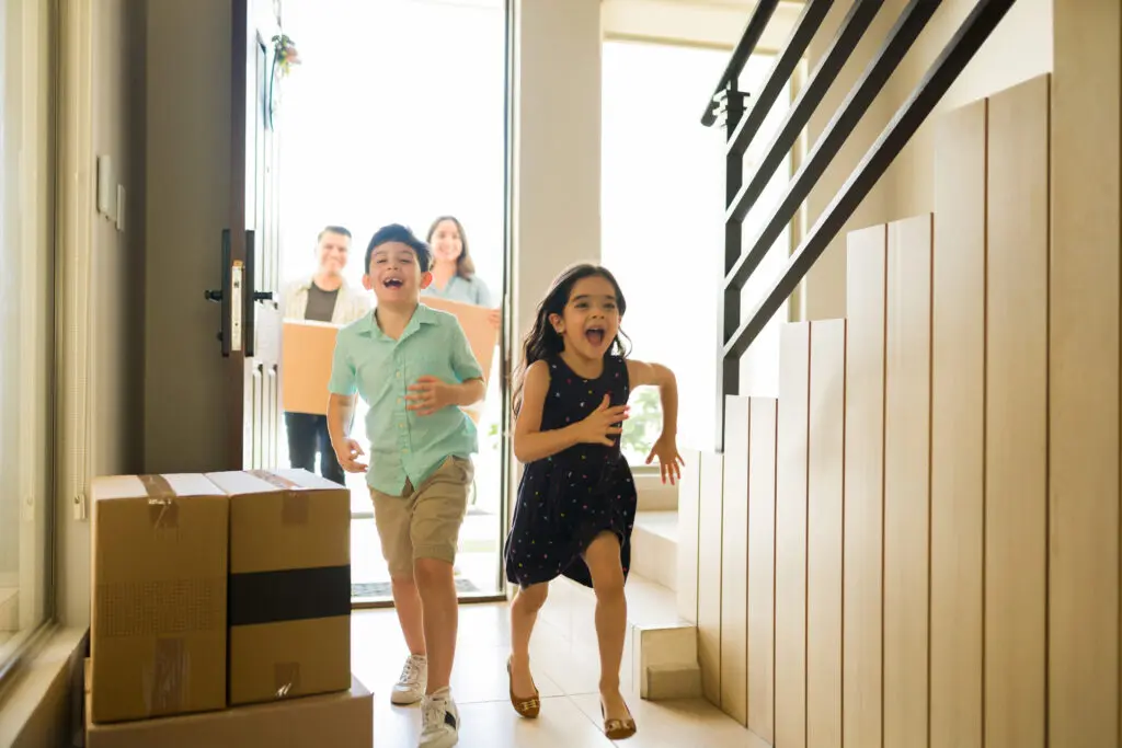 Happy children running and looking excited about moving into a new house with parents carrying moving boxes