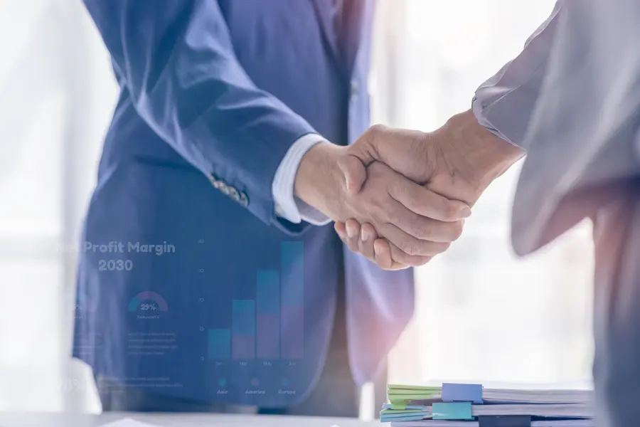 Two business leaders shake hands in a modern office setting