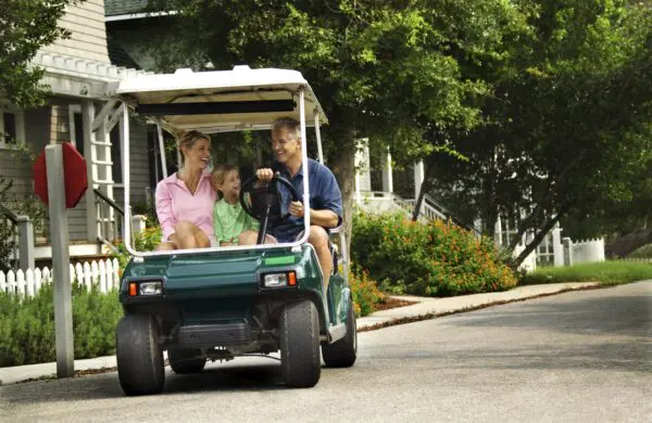 Family of parents and child riding in a golf cart down a street in a residential neighborhood