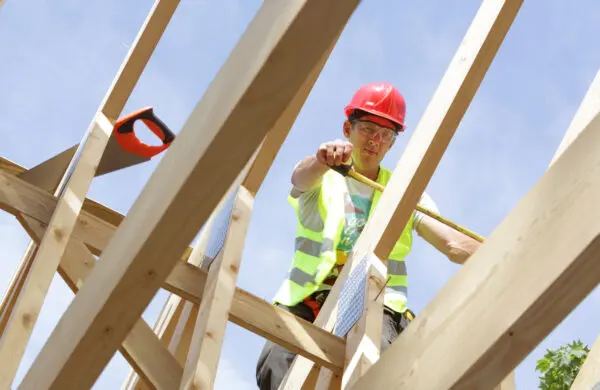 Builder working on roof of house while wearing a hard hat and safety vest