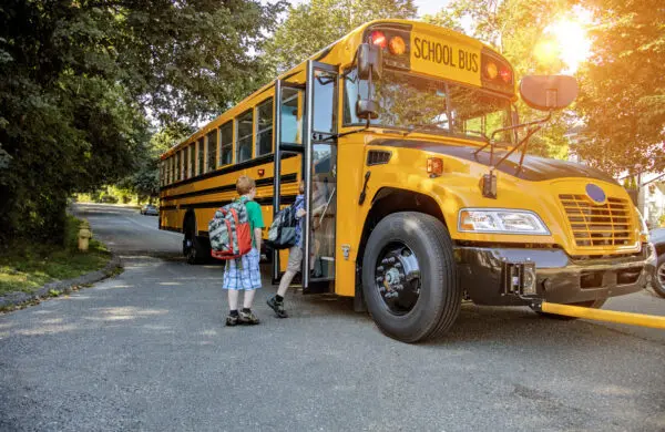 Two young boys in backpacks boarding a school bus