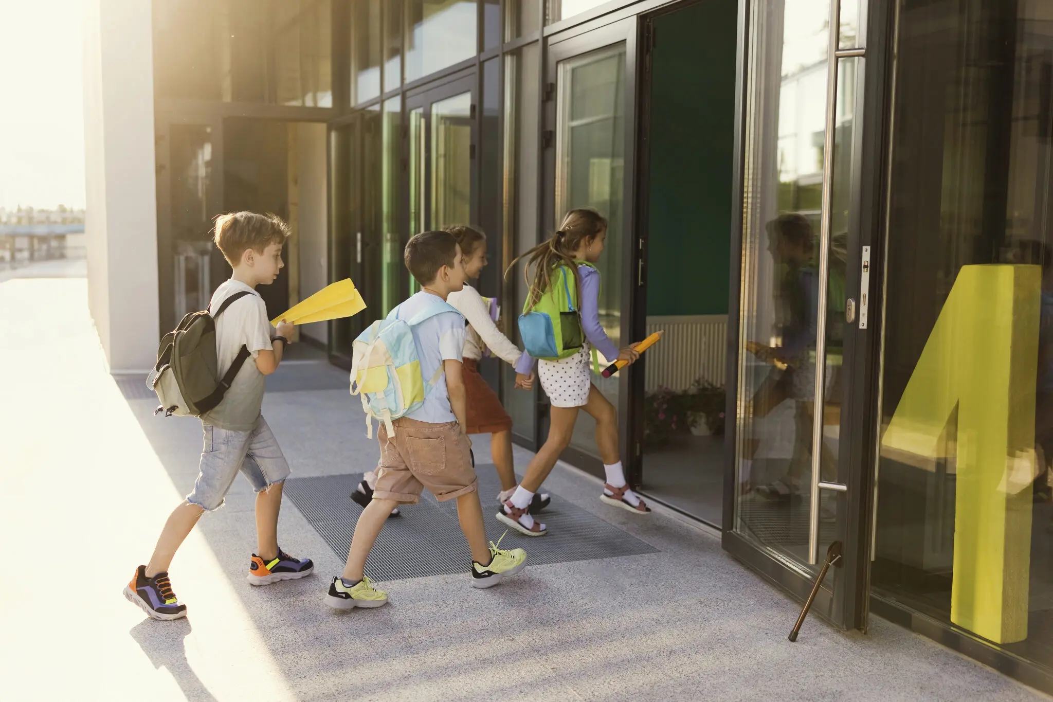 Four children walking into a school building with their backpacks on