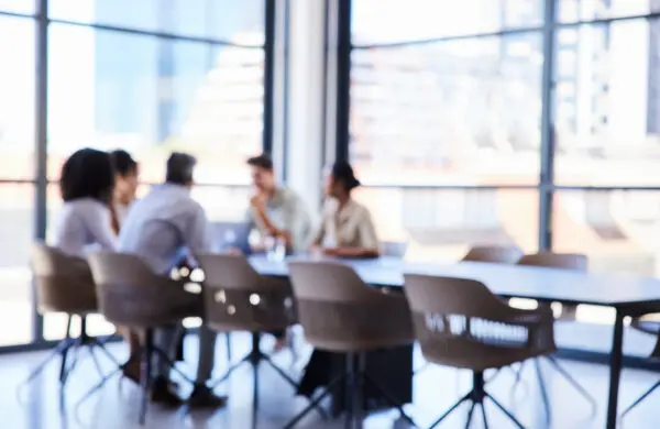 Defocused group of a unrecognizable businesspeople having a meeting together around a table in the boardroom of an office