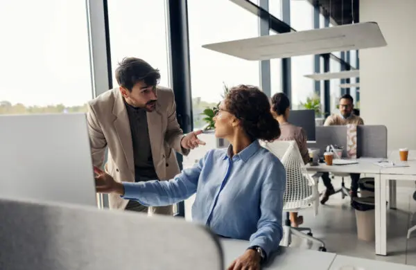 Two business colleagues having an intense discussion or argument in a modern open-plan office setting, pointing at a computer screen