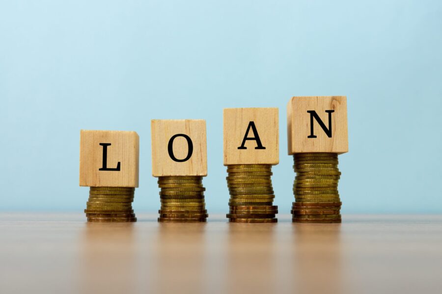 Wooden blocks spelling out the word loan sitting on top of stacks of gold coins
