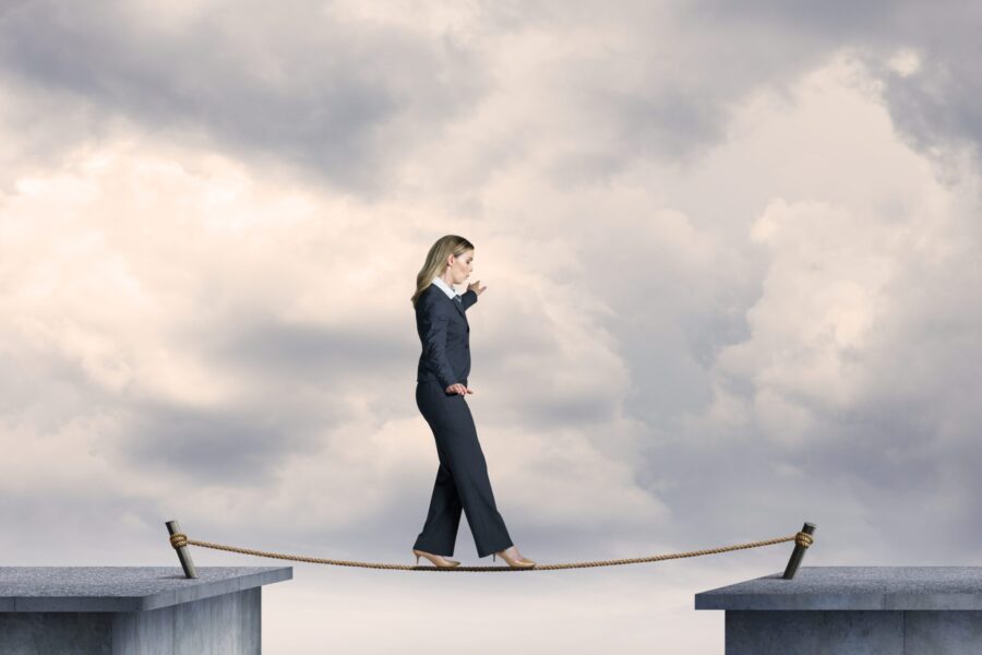 Businesswoman in a suit cautiously walking across a rope bridge between two platforms