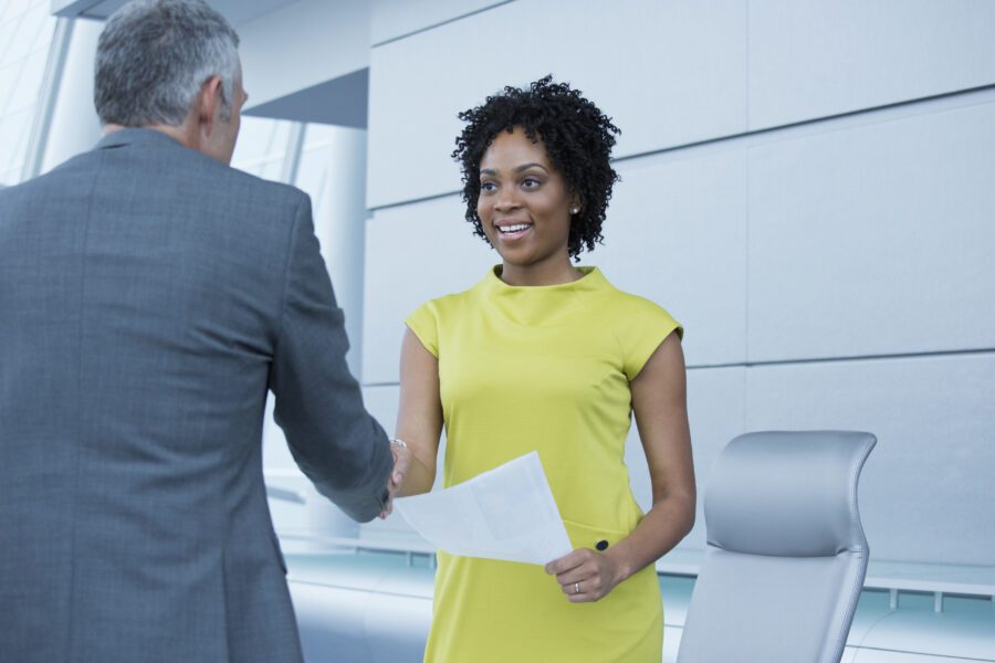 Cheerful professional woman shaking hands with a businessman while holding documents