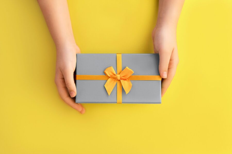 Two hands holding a neatly wrapped gift box with a yellow ribbon on it