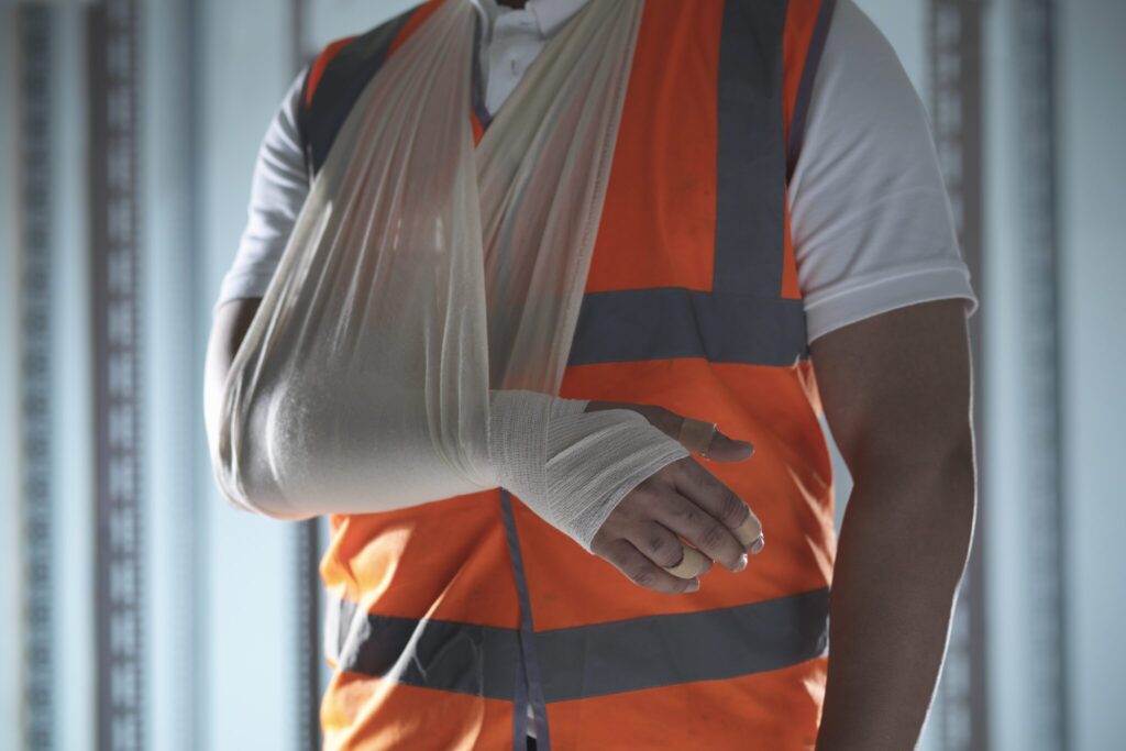 Injured worker wearing a high visibility orange construction vest with his bandaged arm in a sling