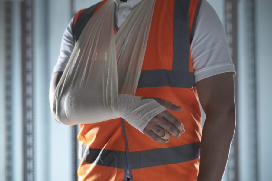 Injured worker wearing a high visibility orange construction vest with his bandaged arm in a sling