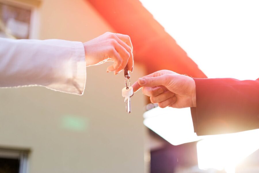 Two hands exchanging house keys in front of a recently sold home