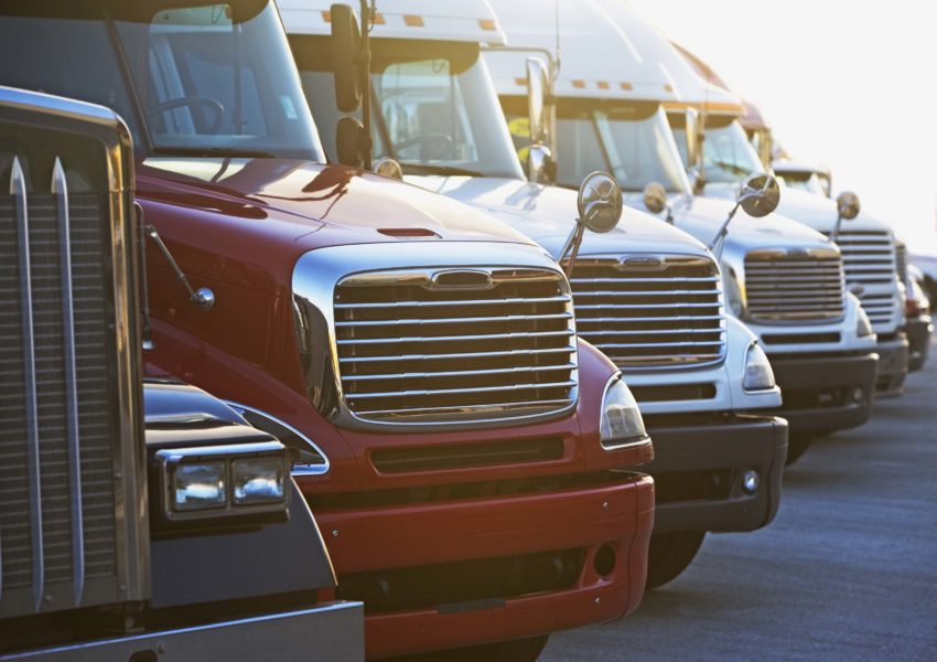 A row of parked semi-trucks lined up in a parking lot