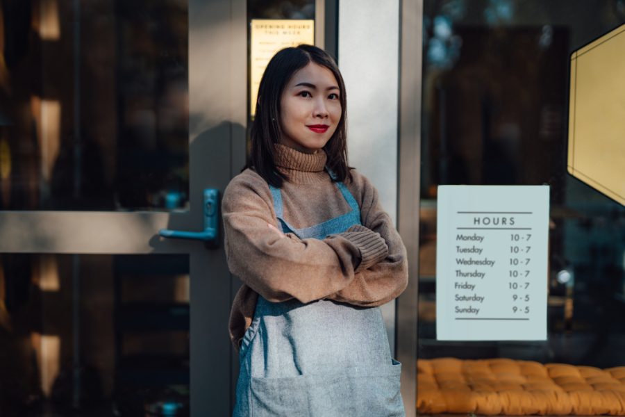 Woman-standing-outside-business-with-open-and-close-hours-sign