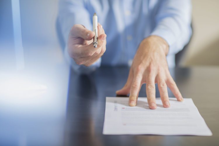 Man holding pen pushing over paper and pen in hand.