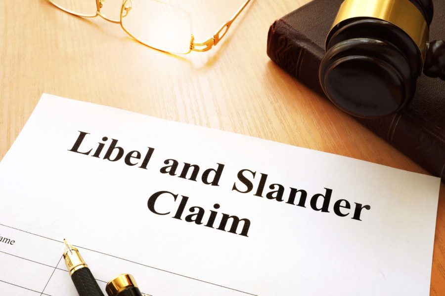 A legal document titled "Libel and Slander Claim" on a desk next to a gavel and glasses