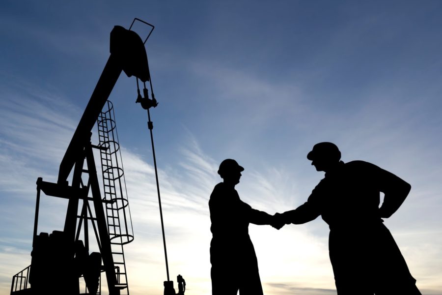 Silhouettes of oil and gas industry workers shaking hands near a pumpjack