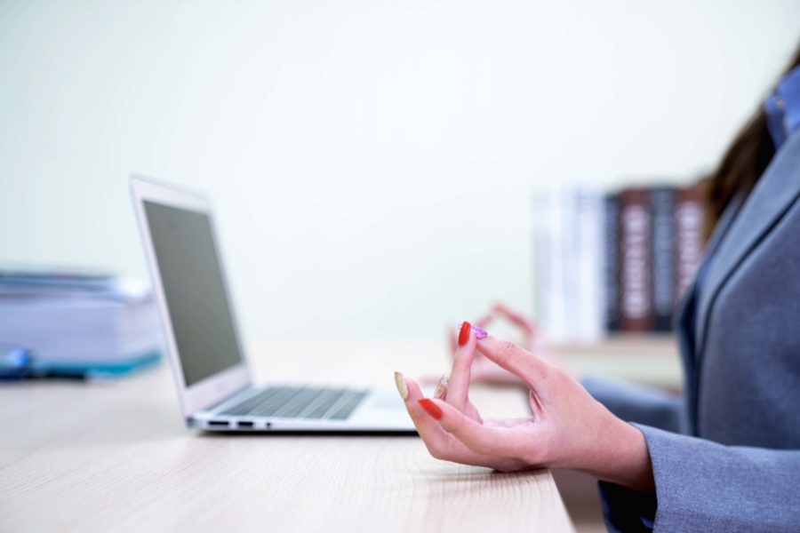 A businesswoman meditating at her desk with her laptop open