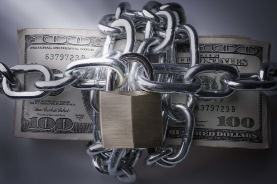 A stack of $100 bills wrapped in metal chains and secured with a padlock