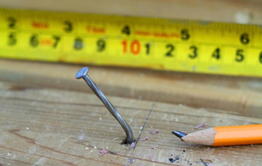 A bent nail in a wooden plank with a broken pencil and measuring tape next to it