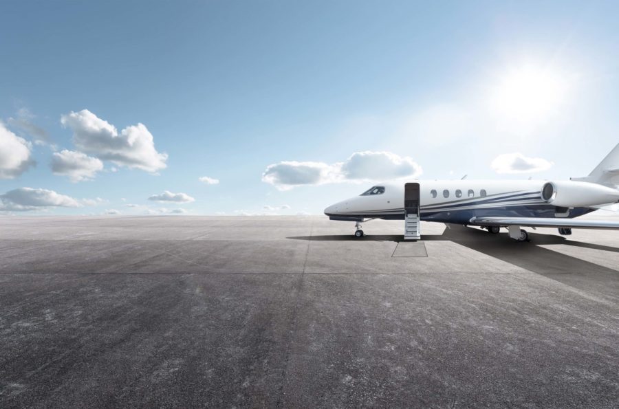 A private jet parked on an open airport runway under a bright blue sky with scattered clouds