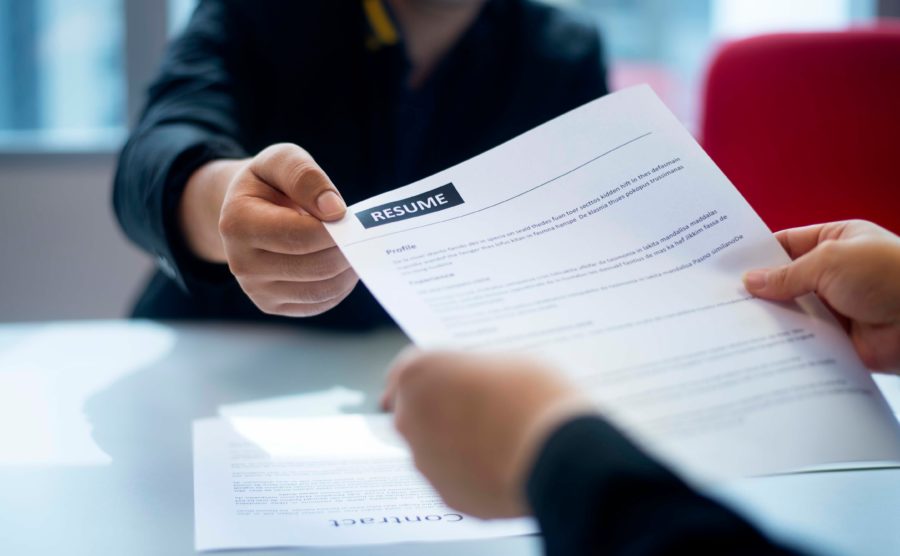 Two people exchanging a resume across a table, one hand passing the document while the other receives it. As their conversation unfolds, they ponder insightful questions to ask references, ensuring a thorough understanding of the candidate's potential.