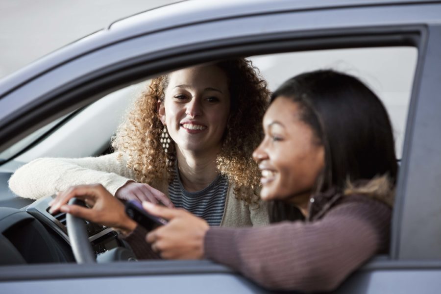 Two young teens sitting in a parked car and smiling with enjoyment