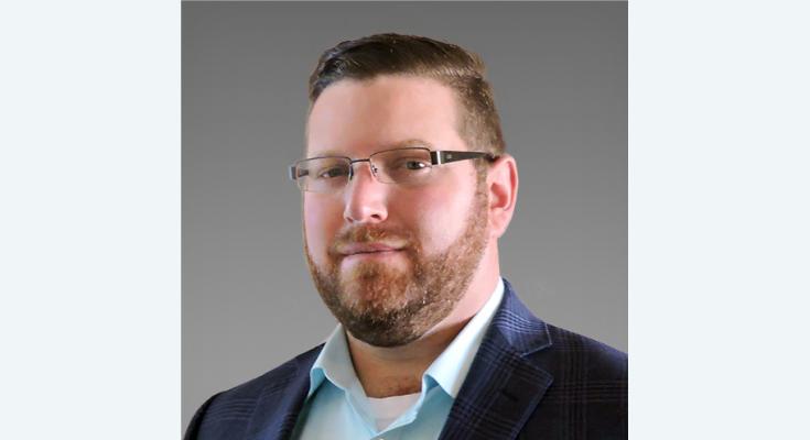 Brian Toglia, a man with short hair, glasses, and a beard, dons a blue shirt and dark jacket. Seen against a gray background, Brian exemplifies the expertise of Higginbotham's Life Science Practice.