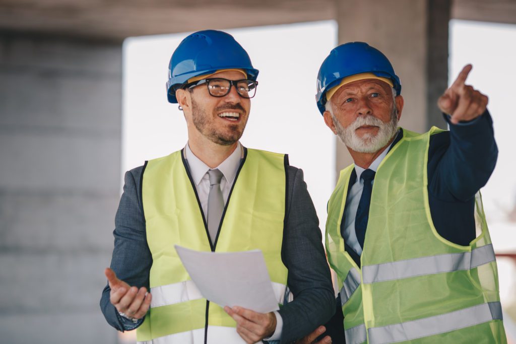 younger and older man in vests and hard hats