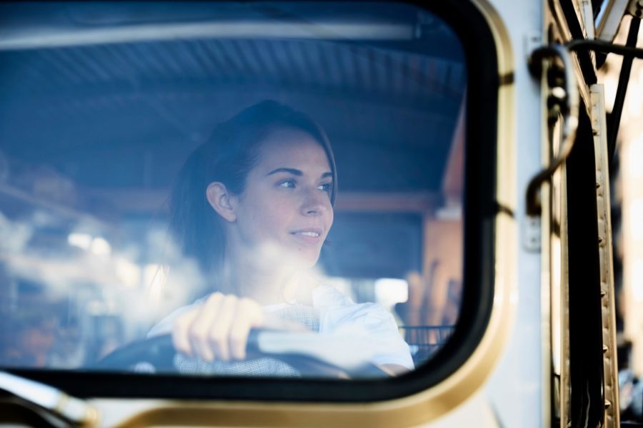A person is sitting in the driver's seat of a vehicle, looking out the window with a slight smile. The interior and part of the steering wheel are visible, perhaps contemplating the benefits of commercial truck insurance for their journey ahead.