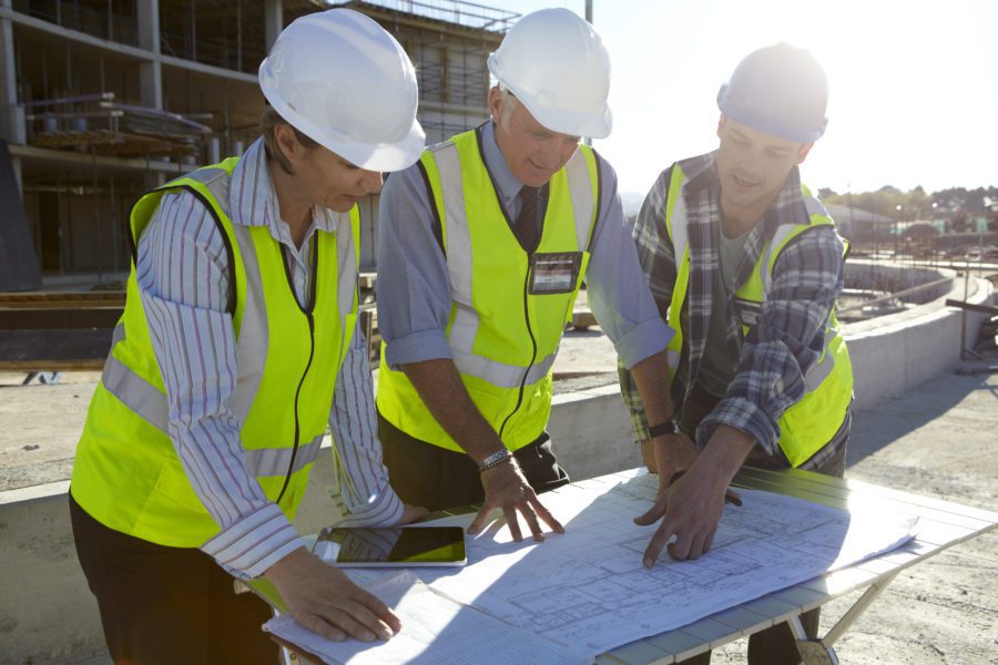 Three construction professionals reviewing building blueprints at a project site