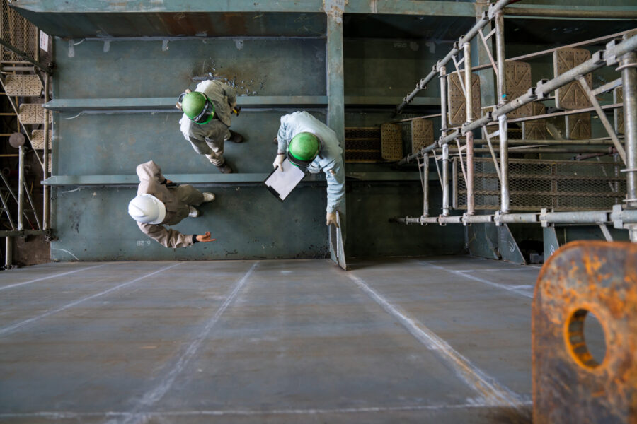 Overhead View Of Three Engineers Discussing Progress Of A Shipbuilding Project