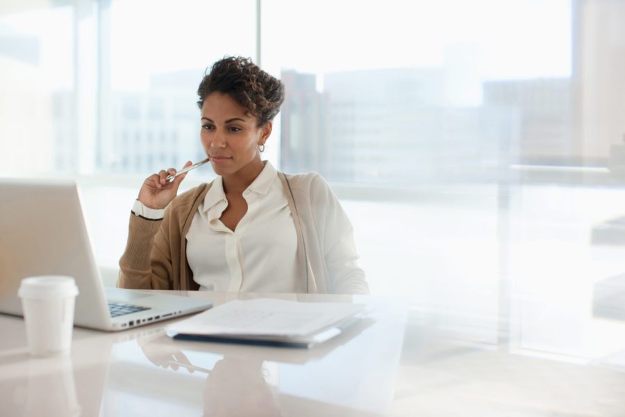 Smiling businesswoman sitting at her desk reviewing notes on her laptop
