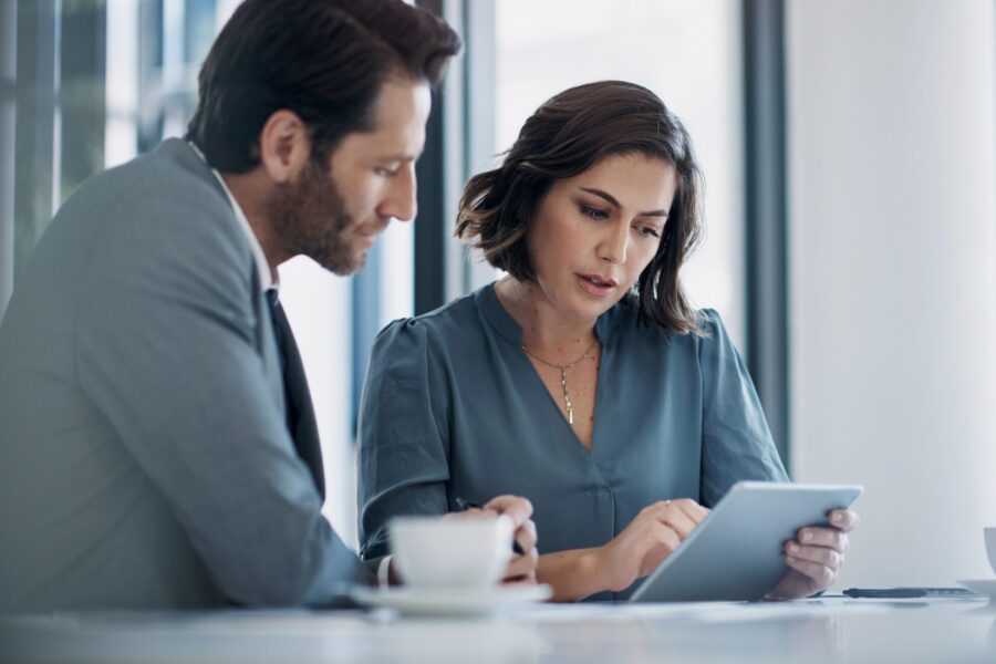 Business Man, Woman And Tablet In Discussion For Deal, Agreement And Proposal For B2b Collaboration. People, Touchscreen And Meeting With Review For Financial Strategy, Stats Or Negotiation In Office