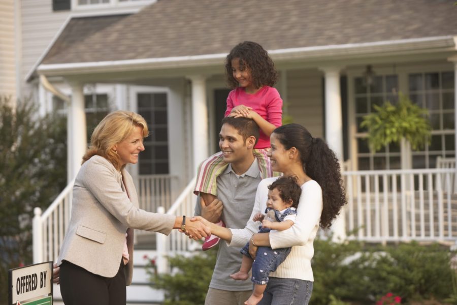 Happy family standing outside their new home and shaking hands with a real estate agent