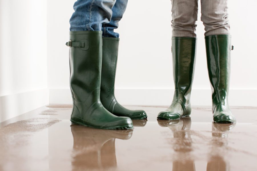 Two people in green rubber boots stand on a wet, reflective floor indoors, facing each other, as if discussing the importance of water sewer backup coverage.
