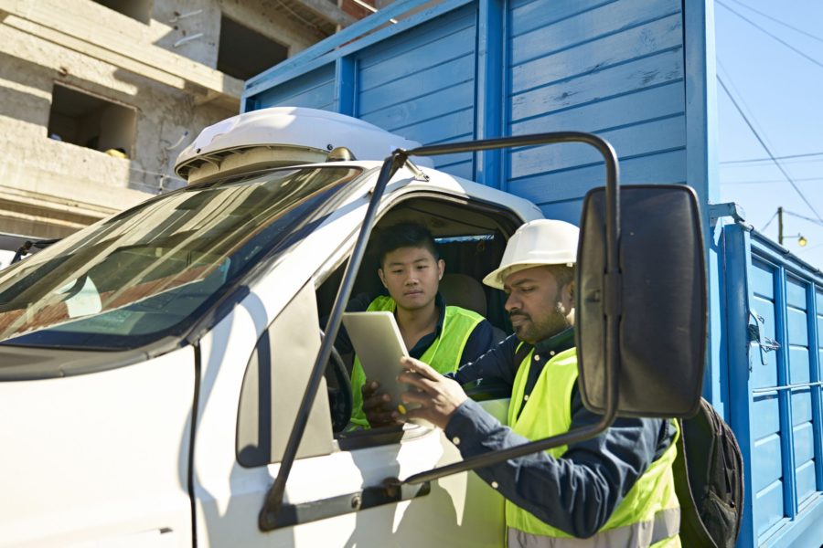 Male construction workers examining checklist on digital tablet on sunny day. Building contractors are discussing at construction site. They are wearing hardhats.