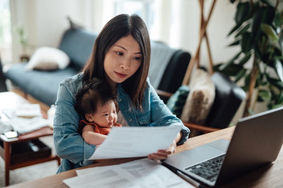 A mother holding her baby while reviewing documents in the comfort of her home