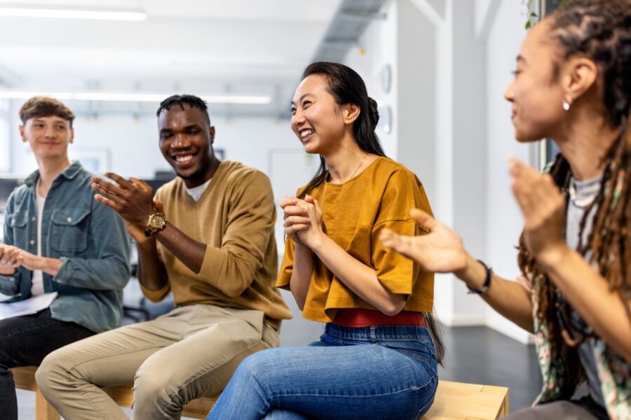 Multiracial business team applauding after a successful staff meeting. Group of business people sitting in a circle clapping hands in meeting.