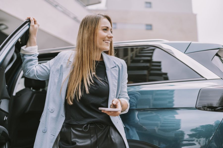 Happy woman with mobile phone standing by car door