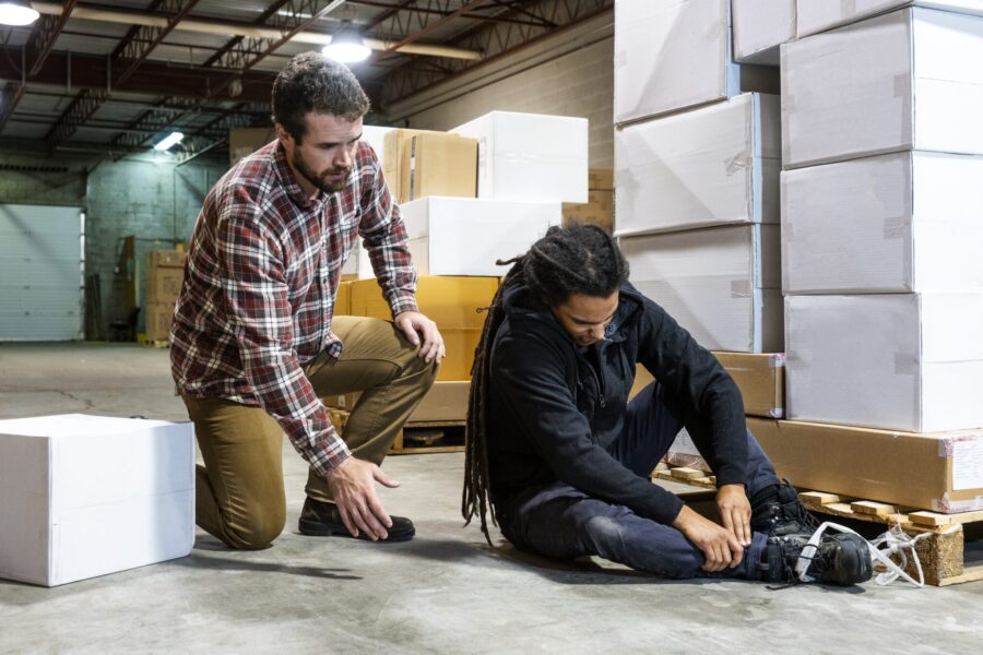 A warehouse worker injured after falling beside a pallet. His boot caught in some plastic wrapping cause him to have an accident. A coworker has come to his assistance.