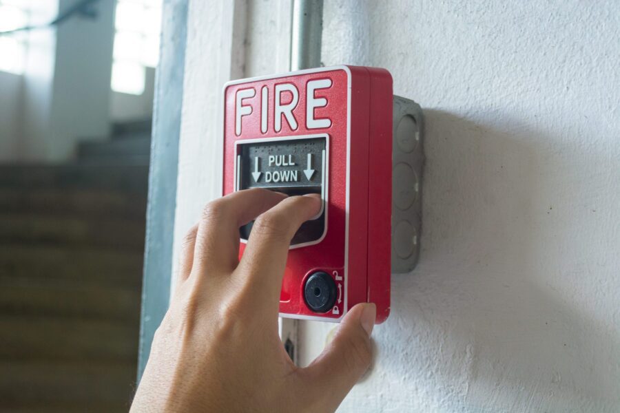 Fire alarm switch, The hand of man is pulling fire alarm on the wall next to the door,Fire alarm switch.Break glass and press button to activate. With hand and direction arrow, Hand push fire botton.