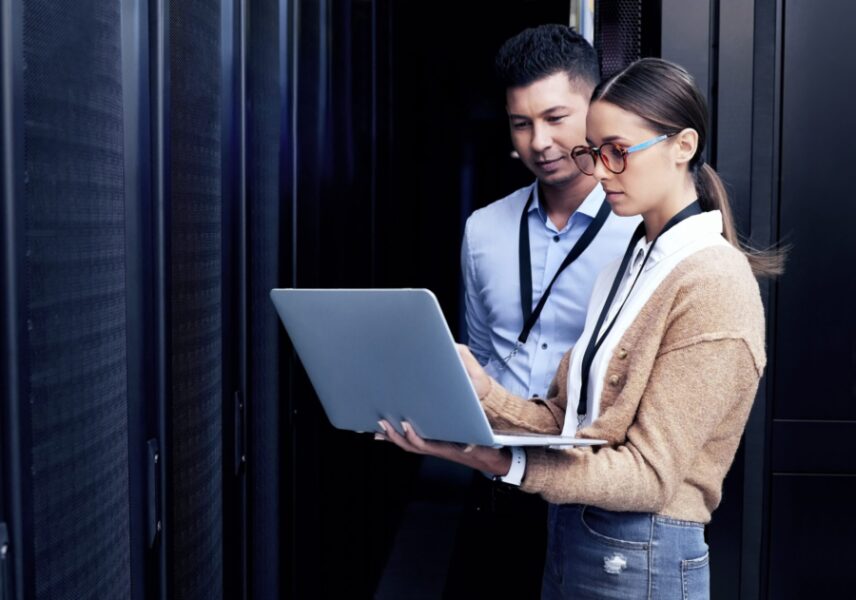 Two IT professionals standing in an office reviewing data together on a laptop