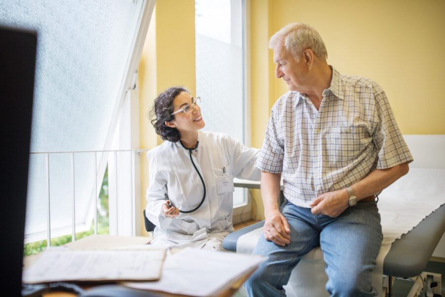 Female doctor examining senior male patient at her clinic. Medicine professional diagnosing elderly man in medical examination room.