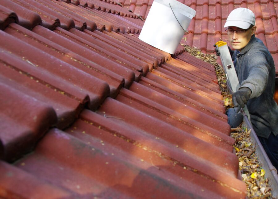 The man on ladder cleans the gutters on the roof. Spring and autumn problem with leaves in gutter.