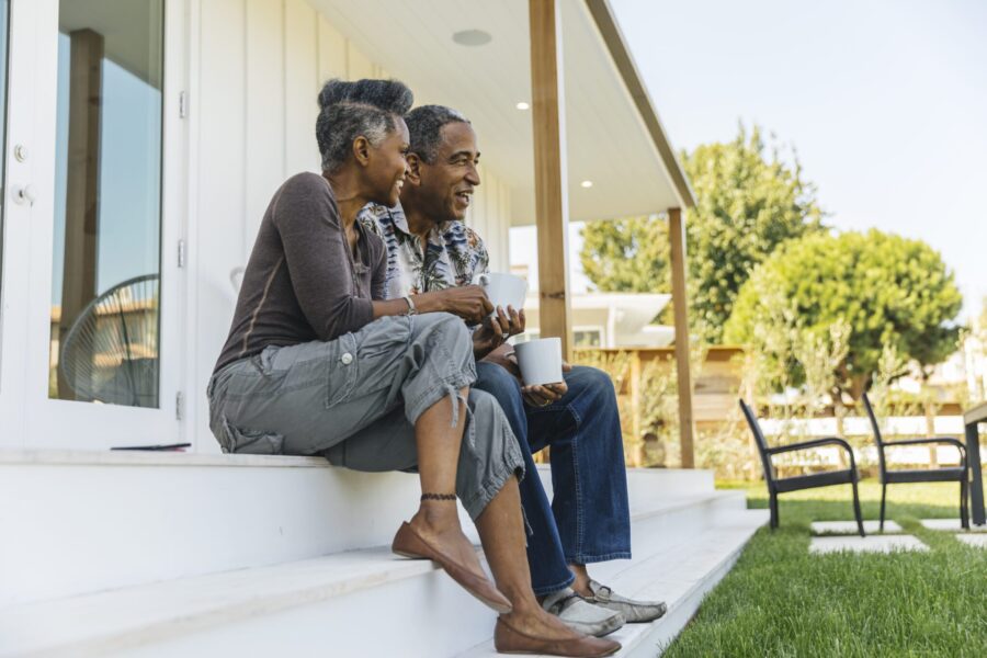 Smiling senior couple sitting on their porch and enjoying a cup of coffee on a sunny morning