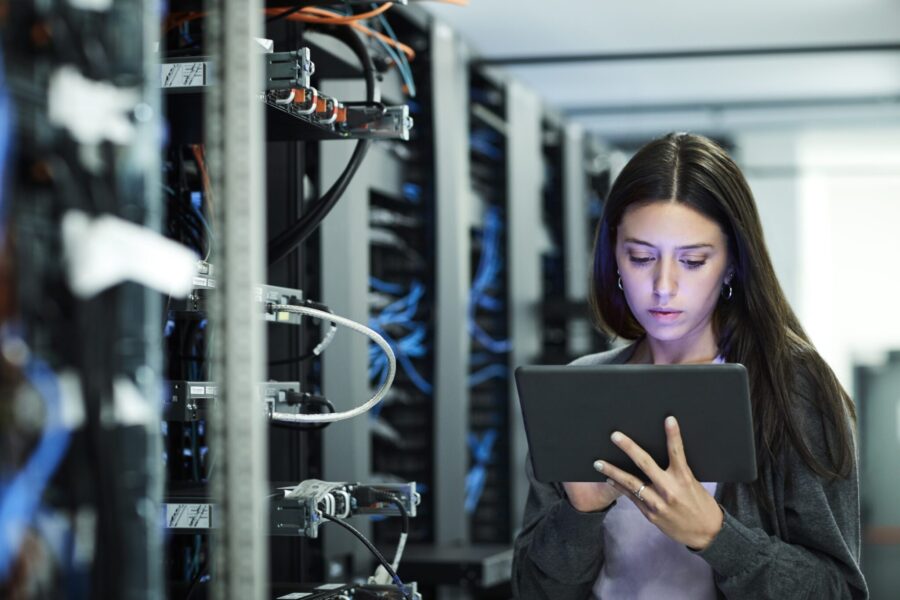 Female technician using digital tablet in server room. IT professional is standing at workplace. She is in casuals.