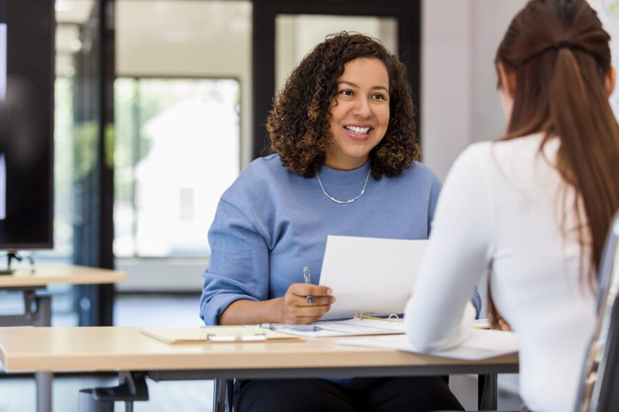 The office manager holds onto a resume while speaking with the new intern they are considering.